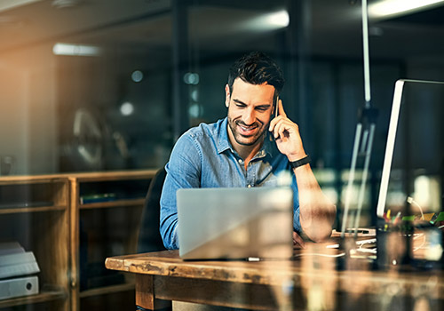Man on his cell phone while working on lap top in cafe